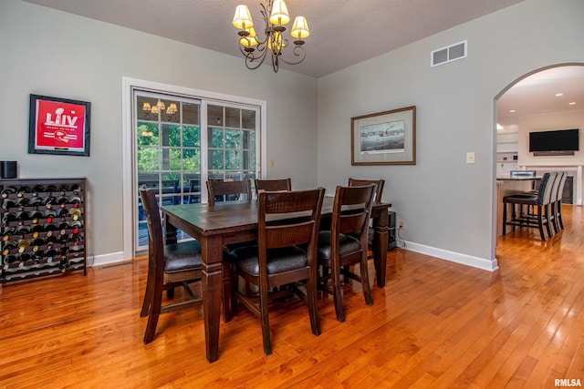 dining space featuring light wood-type flooring, a textured ceiling, and a notable chandelier