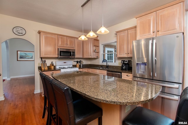 kitchen with sink, a center island, stainless steel appliances, light brown cabinets, and decorative light fixtures