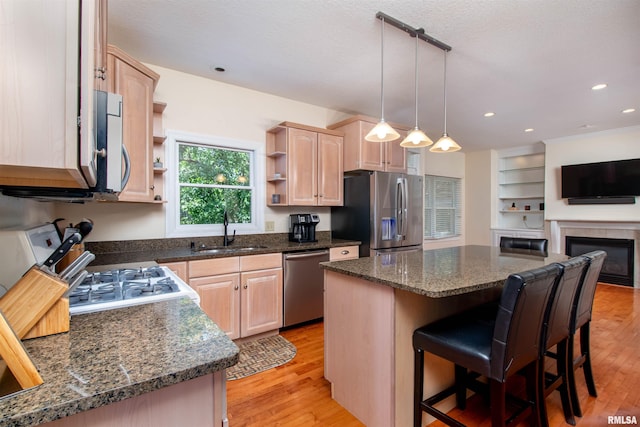 kitchen featuring appliances with stainless steel finishes, a center island, light brown cabinetry, and sink