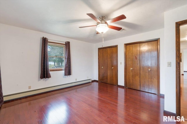 unfurnished bedroom featuring ceiling fan, dark hardwood / wood-style flooring, baseboard heating, and multiple closets