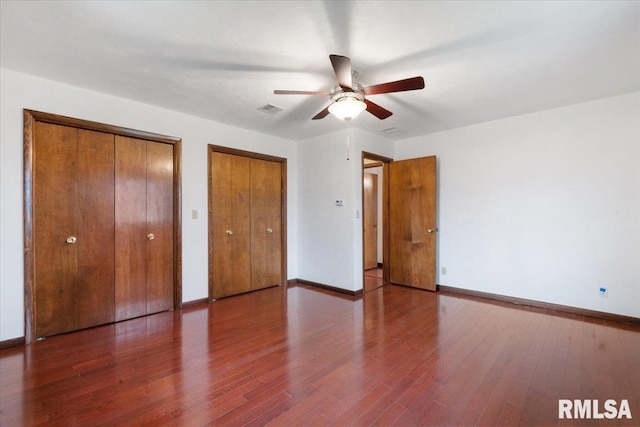 unfurnished bedroom with ceiling fan, dark wood-type flooring, and multiple closets