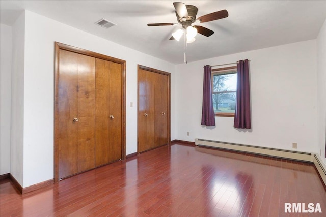 unfurnished bedroom with ceiling fan, a baseboard radiator, two closets, and wood-type flooring