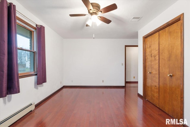 unfurnished bedroom featuring ceiling fan, a closet, dark wood-type flooring, and a baseboard heating unit