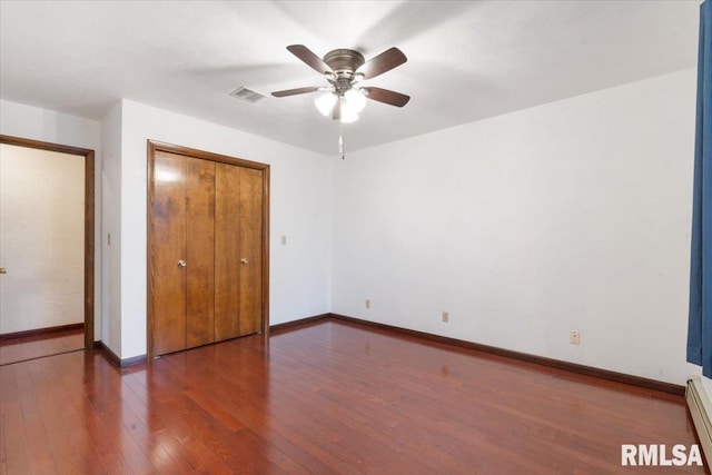 unfurnished bedroom featuring baseboard heating, dark hardwood / wood-style flooring, ceiling fan, and a closet