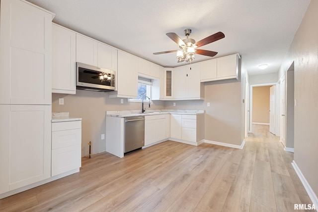 kitchen with appliances with stainless steel finishes, ceiling fan, sink, white cabinets, and light hardwood / wood-style floors