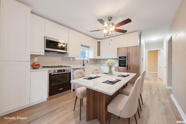 kitchen with stainless steel appliances, sink, white cabinets, light hardwood / wood-style floors, and a breakfast bar area