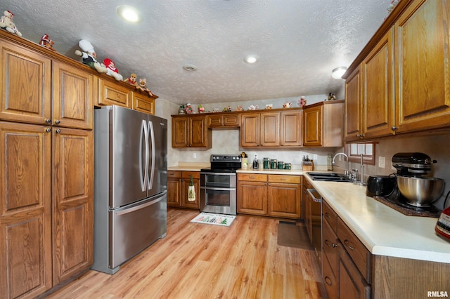 kitchen featuring a textured ceiling, light wood-type flooring, sink, and appliances with stainless steel finishes