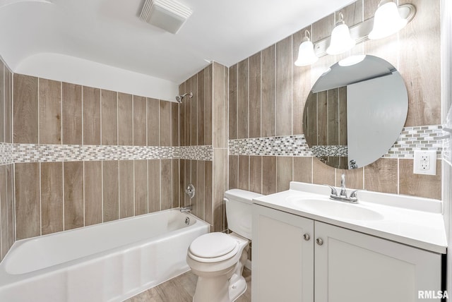 full bathroom featuring tiled shower / bath combo, wood-type flooring, toilet, vanity, and tile walls