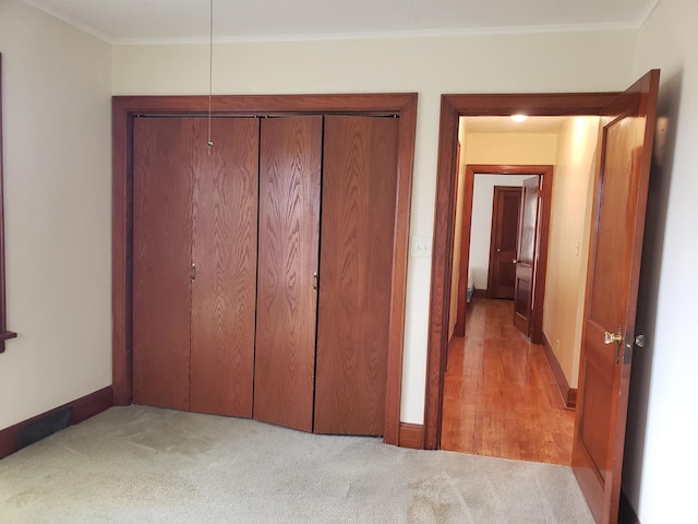 unfurnished bedroom featuring light colored carpet, ornamental molding, and a closet