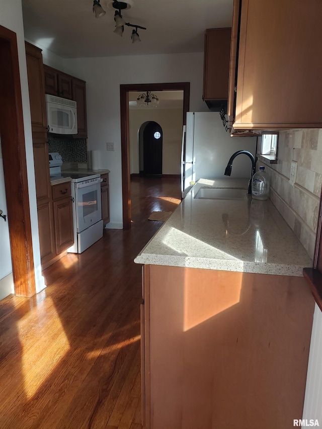 kitchen with dark wood-type flooring, sink, light stone counters, white appliances, and decorative backsplash