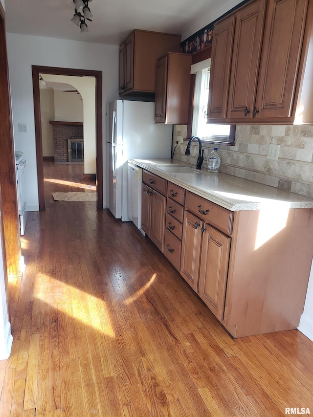 kitchen featuring dishwasher, sink, backsplash, hardwood / wood-style flooring, and a brick fireplace