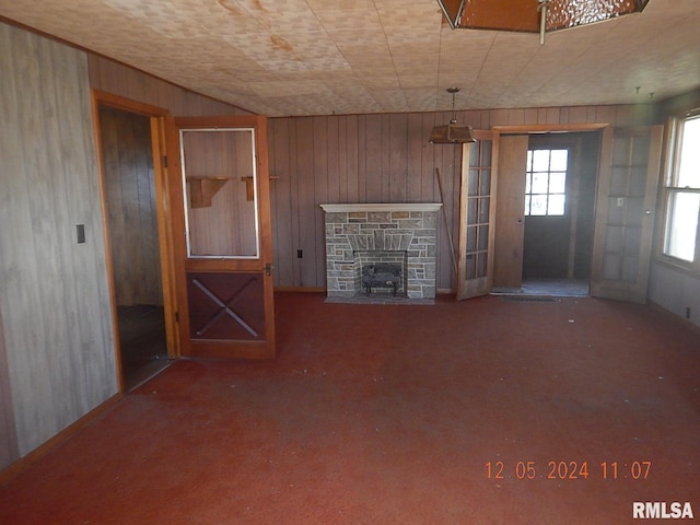 unfurnished living room featuring wood walls, a stone fireplace, and carpet floors