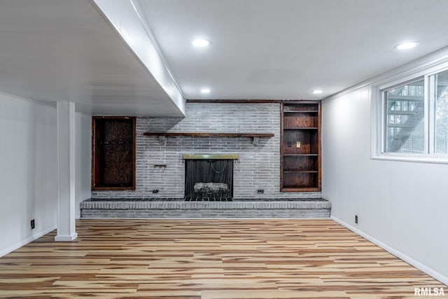 unfurnished living room featuring built in shelves, light wood-type flooring, and a brick fireplace