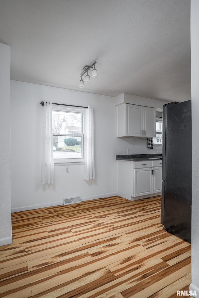 kitchen with rail lighting, light hardwood / wood-style floors, black fridge, and white cabinetry