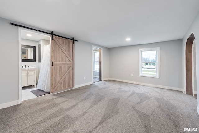 unfurnished bedroom with a barn door, light colored carpet, sink, and ensuite bath