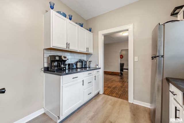 kitchen featuring white cabinets, light wood-type flooring, backsplash, and stainless steel refrigerator