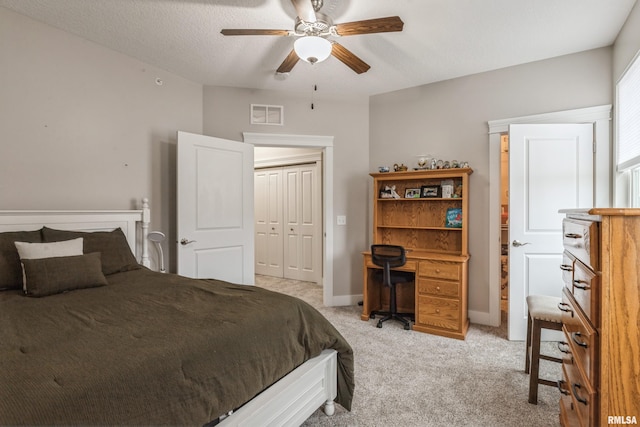 bedroom featuring ceiling fan, a closet, light carpet, and a textured ceiling