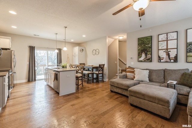 living room featuring ceiling fan, light wood-type flooring, and a textured ceiling