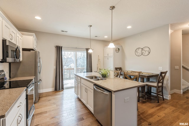 kitchen with appliances with stainless steel finishes, sink, a center island with sink, white cabinetry, and hanging light fixtures