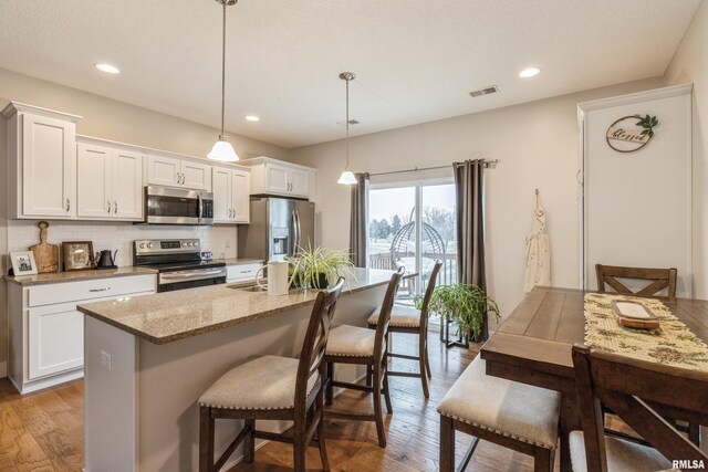 kitchen with white cabinets, an island with sink, pendant lighting, and appliances with stainless steel finishes