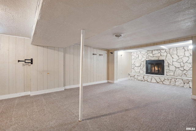 basement with carpet flooring, a textured ceiling, a stone fireplace, and wood walls