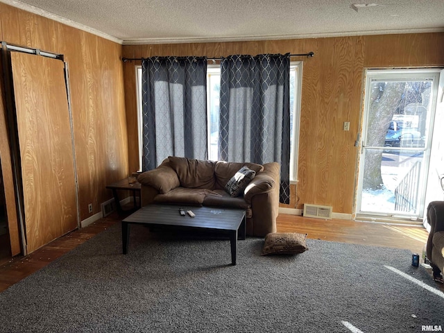 living room featuring crown molding, hardwood / wood-style flooring, wooden walls, and a textured ceiling