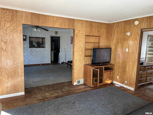 unfurnished living room with dark wood-type flooring, wooden walls, crown molding, and a textured ceiling