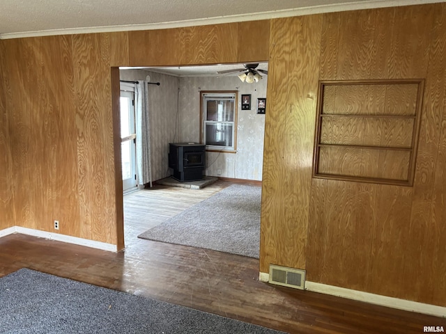 560 4th Ave S, Clinton, IA 52732 - unfurnished room featuring a wood stove, wood finished floors, ceiling fan, baseboards, and crown molding