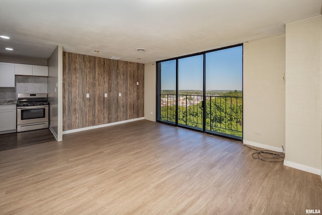 unfurnished living room with floor to ceiling windows, light hardwood / wood-style floors, and wooden walls