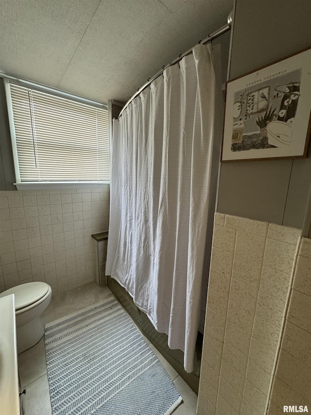 bathroom with tile patterned flooring, toilet, tile walls, and a textured ceiling