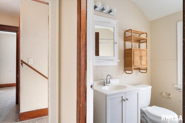 bathroom with vanity, toilet, tile walls, and lofted ceiling