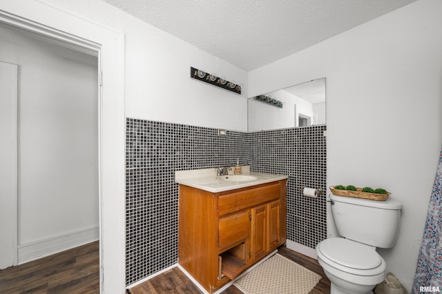 bathroom with vanity, a textured ceiling, wood-type flooring, tile walls, and toilet