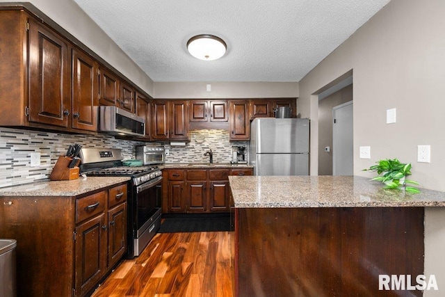 kitchen featuring appliances with stainless steel finishes, backsplash, light stone counters, dark brown cabinets, and dark hardwood / wood-style floors