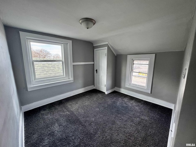 additional living space featuring a healthy amount of sunlight, dark carpet, and lofted ceiling