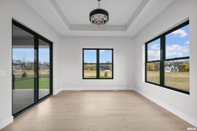 spare room with a notable chandelier, plenty of natural light, light wood-type flooring, and a tray ceiling