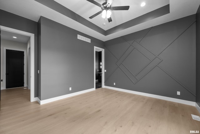 spare room with ceiling fan, light hardwood / wood-style floors, and a tray ceiling