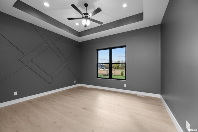 unfurnished room featuring a raised ceiling, ceiling fan, and light hardwood / wood-style floors