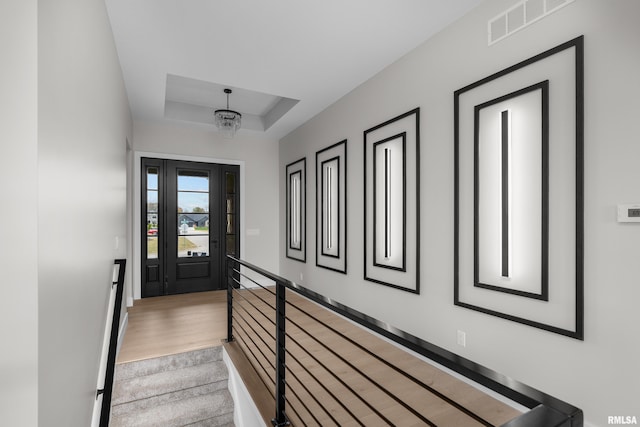 staircase featuring carpet, a tray ceiling, and a chandelier