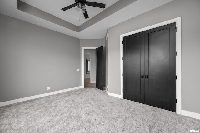 unfurnished bedroom featuring carpet flooring, a closet, a raised ceiling, and ceiling fan