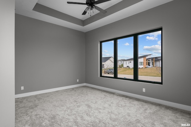 carpeted spare room with a raised ceiling and ceiling fan