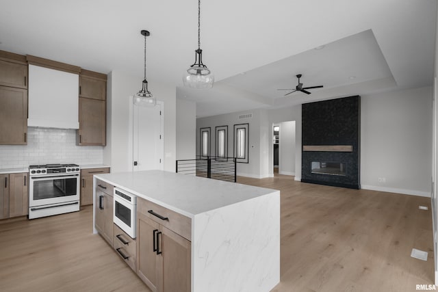 kitchen with a raised ceiling, light hardwood / wood-style floors, a kitchen island, and white gas range