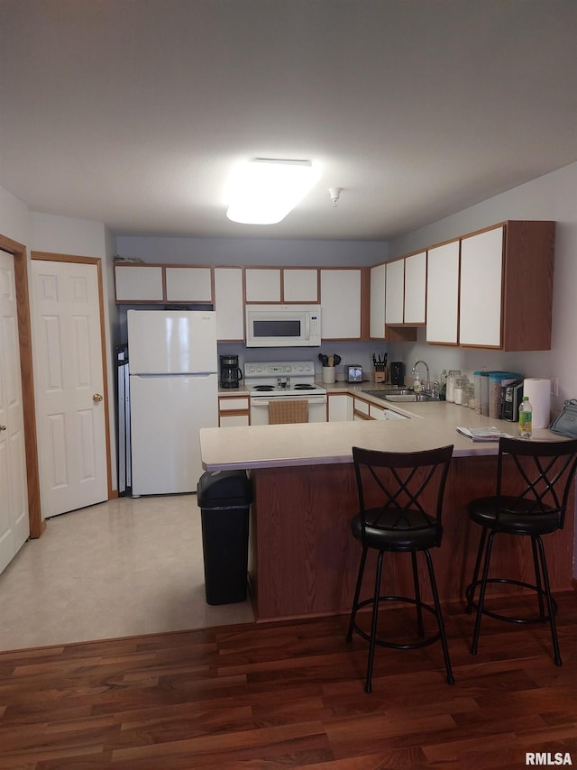 kitchen featuring white cabinetry, sink, kitchen peninsula, white appliances, and a kitchen bar