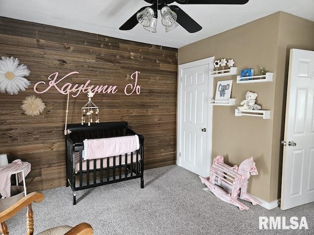 carpeted bedroom featuring ceiling fan, wood walls, and a crib