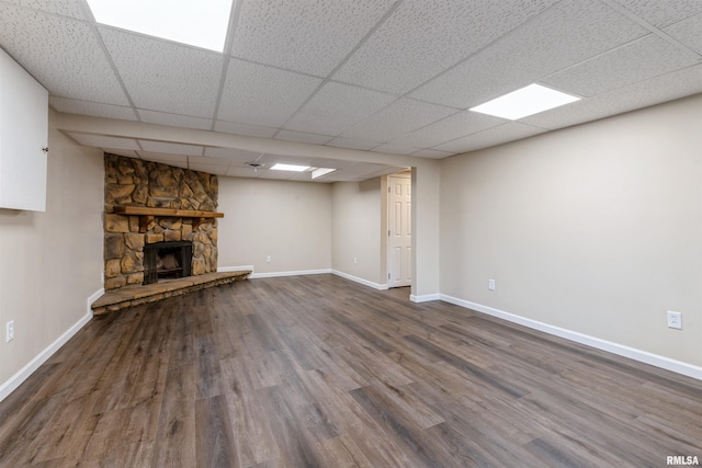 basement with a drop ceiling, a stone fireplace, and wood-type flooring