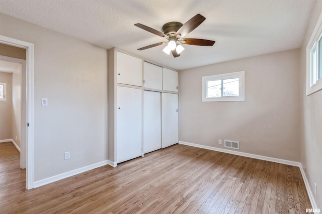 unfurnished bedroom featuring a textured ceiling, a closet, light hardwood / wood-style flooring, and ceiling fan