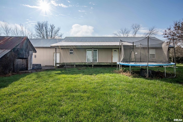 rear view of property featuring a trampoline and a lawn