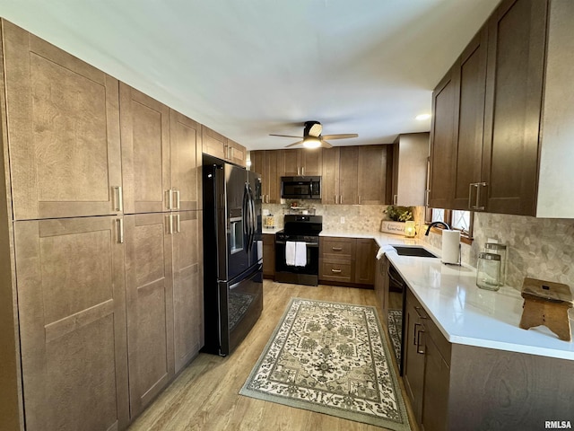 kitchen featuring backsplash, black appliances, sink, light hardwood / wood-style flooring, and ceiling fan