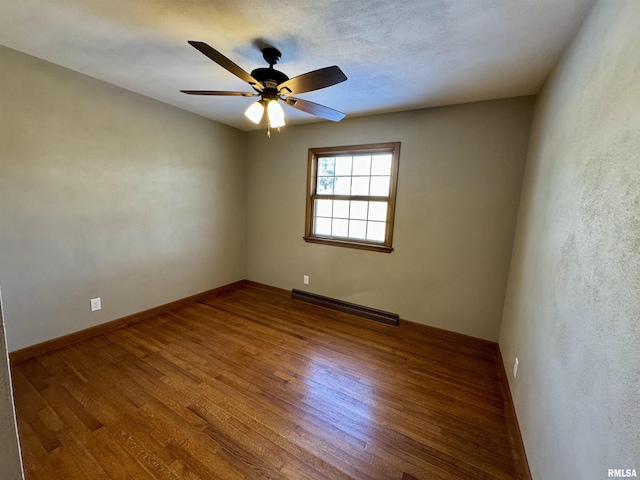 spare room with wood-type flooring, ceiling fan, and a baseboard heating unit