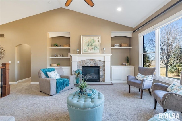 living area with a stone fireplace, lofted ceiling, carpet flooring, and built in shelves