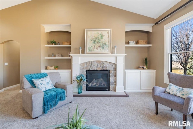 living area featuring built in shelves, carpet, arched walkways, and a wealth of natural light